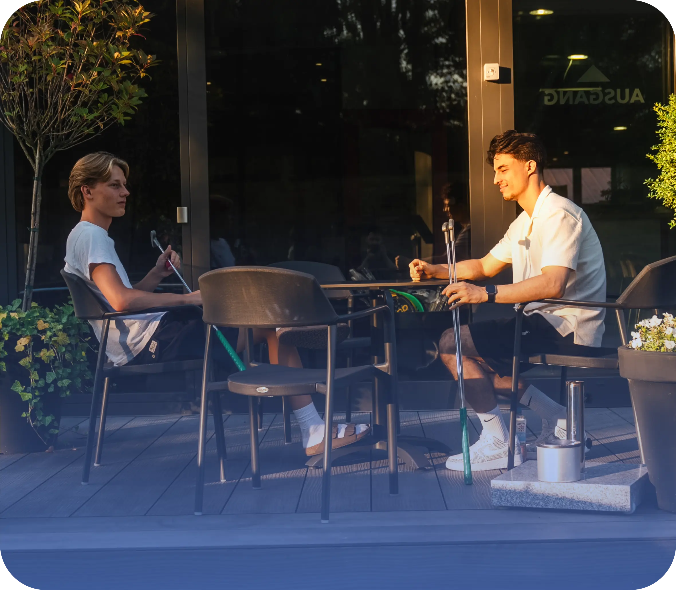 2 Männer sitzen auf der Terrasse mit Minigolfschlägern