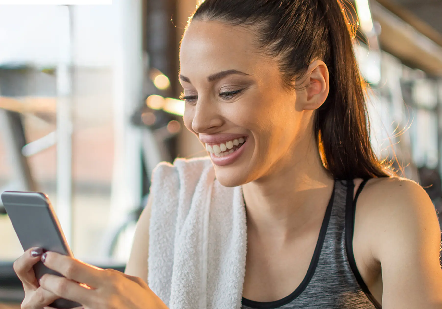 Frau schaut lachend auf ihr Handy im Gym